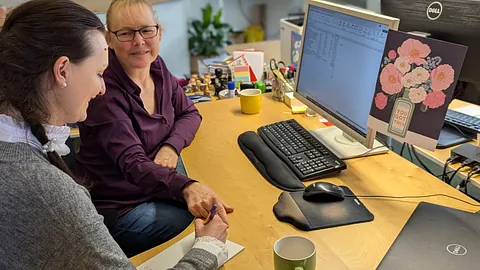 Eine Frau erklärt einer anderen Frau etwas am Computer. Quelle: Emmaus
